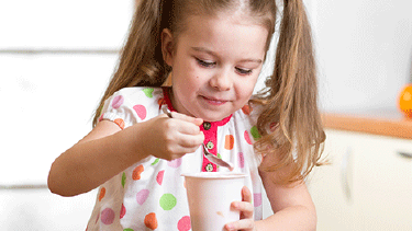 Kleines Mädchen isst genüsslich ein Joghurt.