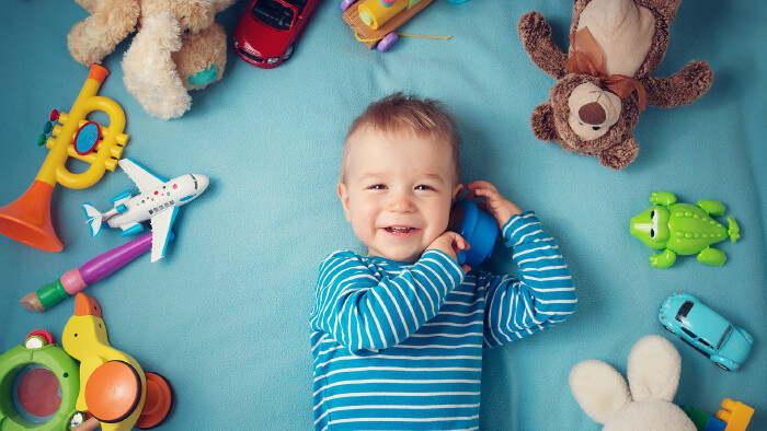 © candy1812, stock.adobe.com Glücklicher einjähriger Bub liegt mit vielen Plüschtieren auf einer blauen Decke