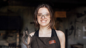 Junge Frau mit Schutzbrille erlernt das Schmiedehandwerk