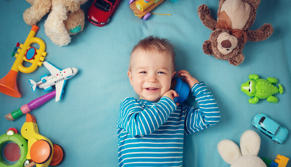 Glücklicher einjähriger Bub liegt mit vielen Plüschtieren auf einer blauen Decke