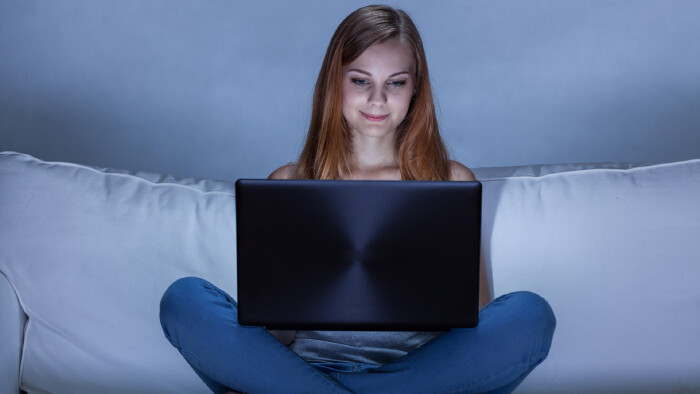 Teenager sitzt mit Laptop auf der Couch