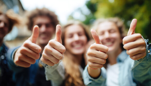 Eine Gruppe fröhlicher junger Erwachsener zeigt Zustimmung und Positivität, indem sie begeistert den Daumen nach oben streckt