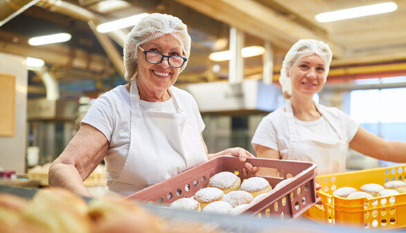 Zwei Bäckerinnen tragen frische Berliner Pfannkuchen in Schachteln.