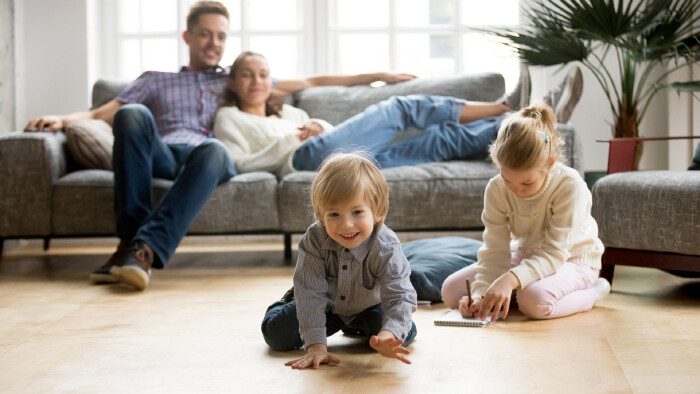 Kinder spielen am Boden w&auml;hrend Eltern vom Sofa aus zusehen