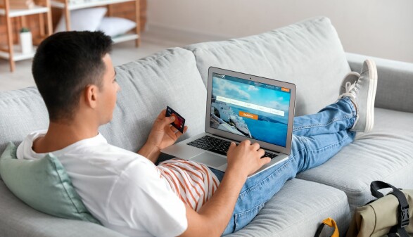 Junger Mann sitzt mit Laptop und Kreditkarte auf der Couch