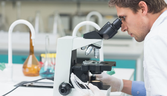 Mann in Laborkleidung blickt durch ein Mikroskop