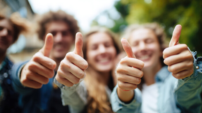 Eine Gruppe fröhlicher junger Erwachsener zeigt Zustimmung und Positivität, indem sie begeistert den Daumen nach oben streckt